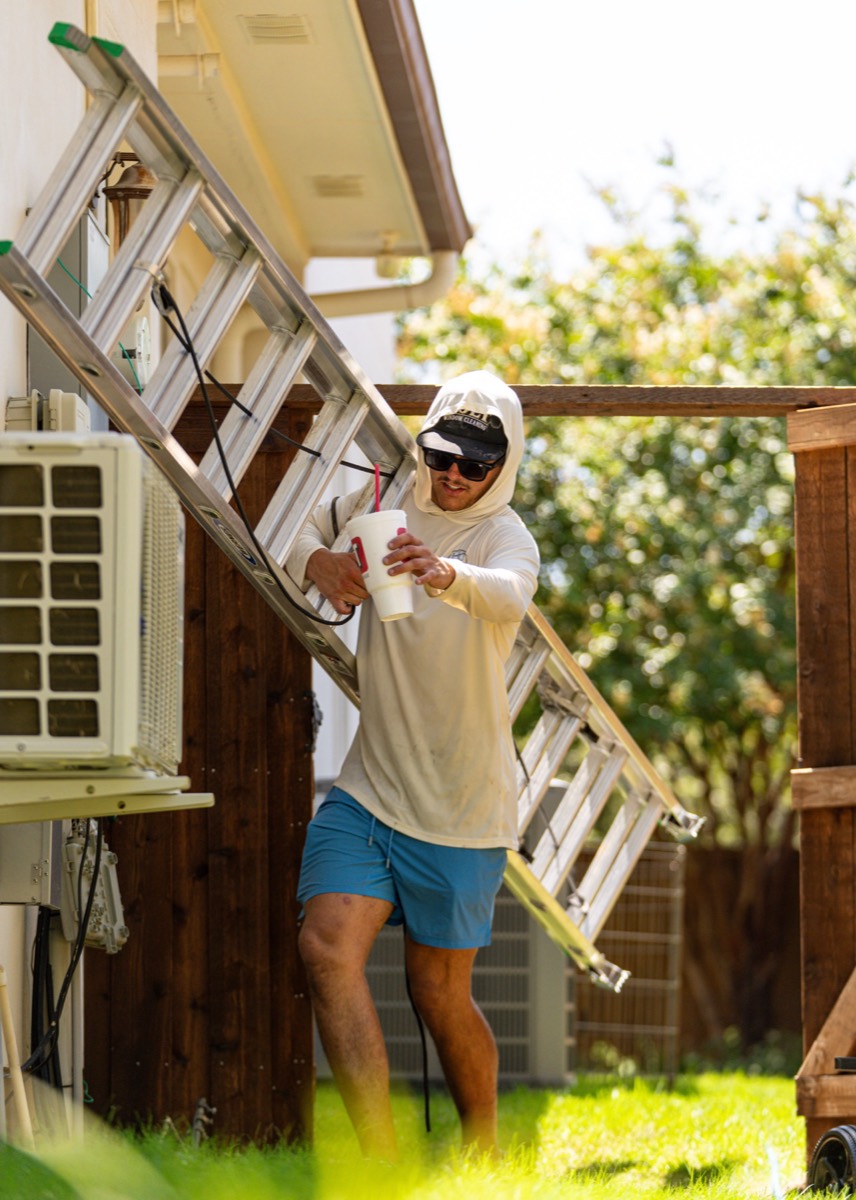 Caleb Holt carrying a ladder through a side yard.